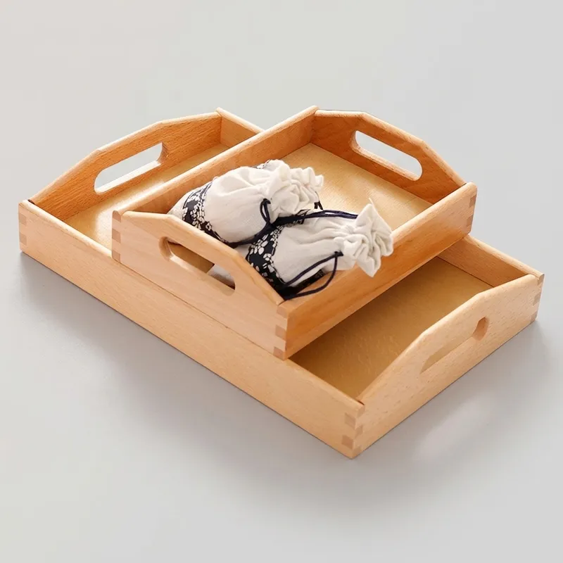 Stacked beech wood serving trays holding fabric drawstring pouches on grey surface